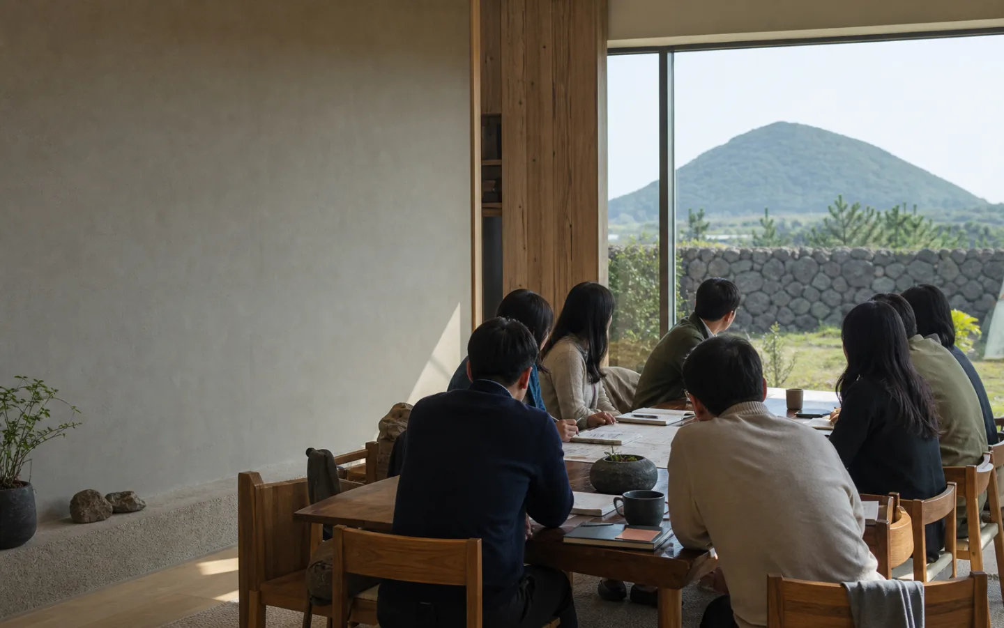 제주 오름과 돌담이 보이는 업무 공간에서 뒷모습으로 회의하는 기업 팀